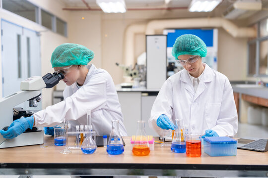 Medical Research Scientist Drops Sample on Slide and Her Colleague Examines it Under Microscope. They Work in a Modern Laboratory.