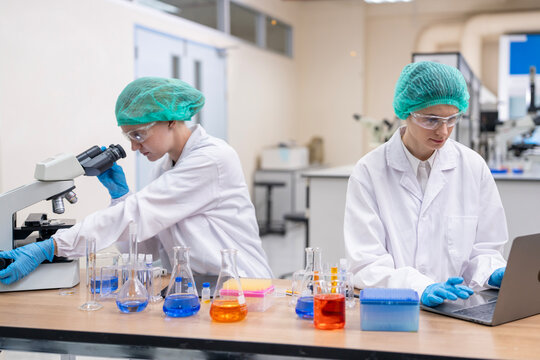 Medical Research Scientist Drops Sample on Slide and Her Colleague Examines it Under Microscope. They Work in a Modern Laboratory.