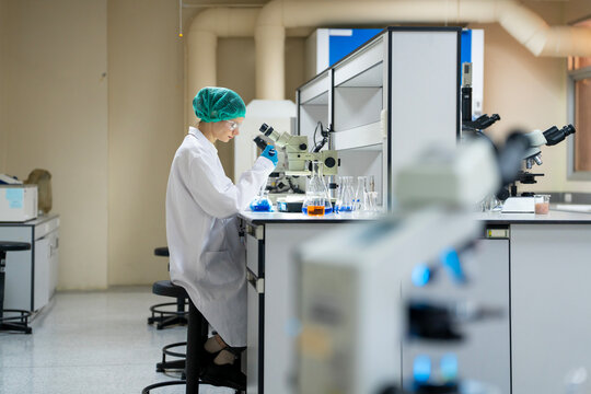 Young female researcher working in the lab, she is examining the samples under a microscope
