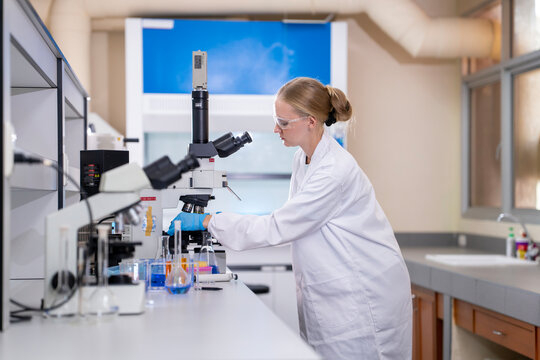 Young female researcher working in the lab, she is examining the samples under a microscope