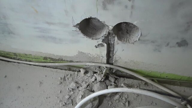 New electrical back box recesses and socket box holes with wiring tunnels drilled into a concrete wall during a house renovation, showing rubble and cables at the construction site