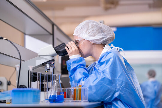 Young female researcher working in the lab, she is examining the samples under a microscope