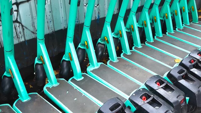 Many turquoise electric scooters neatly parked in a row on a city street, offering a sustainable and eco friendly urban mobility solution for rent through a sharing service app