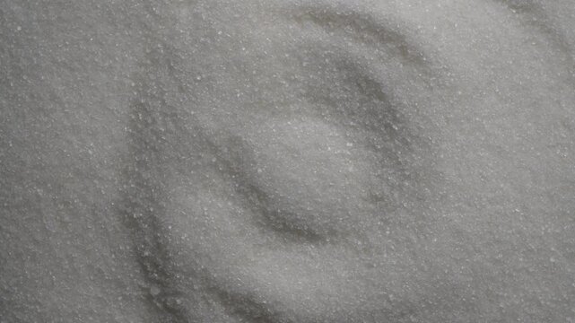 Close up full frame shot of white refined sugar heap forming beautiful abstract wave textures, rotates. Monochromatic food background for baking ingredient, glucose, or sweet design concept