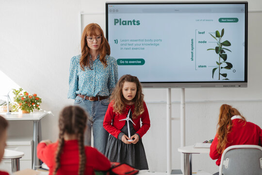 Schoolgirl presenting renewable energy project with model wind turbine in classroom.
