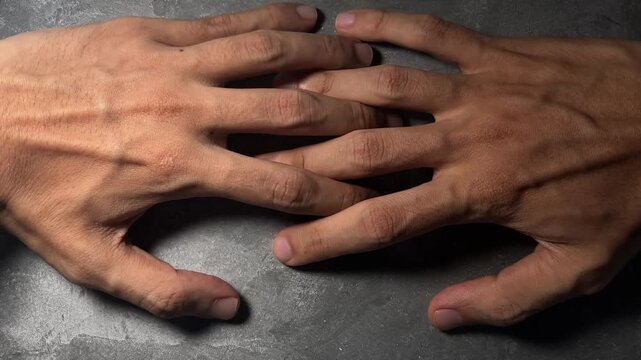 human hands clasped tightly together on grey tabletop