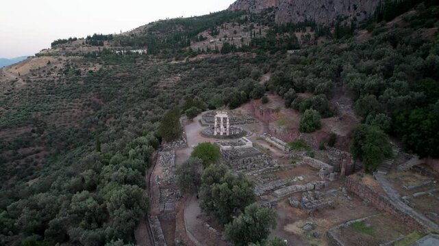 Aerial view of the ancient Tholos of Delphi surrounded by olive trees and rugged mountains in Delphi, Greece.