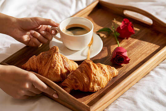 Valentine's Day breakfast tray with croissants, coffee, and roses on a wooden surface