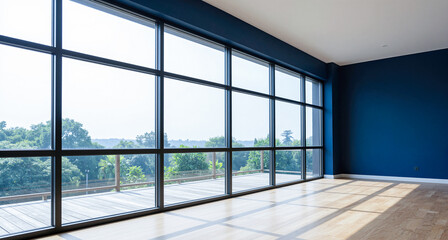 Obraz premium Empty spacious modern room featuring large black framed windows overlooking green trees with dark blue accent wall and wooden parquet floor