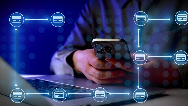 A person uses a smartphone while sitting at a desk with a laptop open. Digital payment symbols appear on the screen, showing connectivity and online transactions.