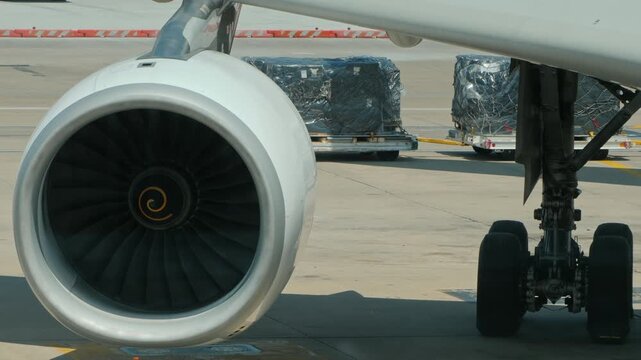 Close up on airplane jet engine and landing gear with cargo containers at airport.