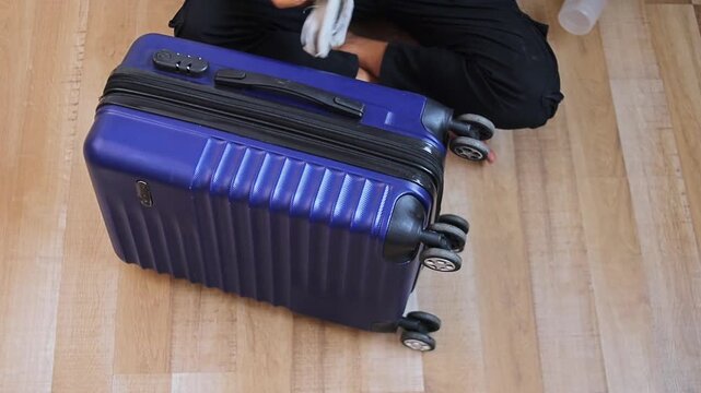 Person cleaning blue hard-shell rolling luggage bag with chamois while sitting on wooden floor