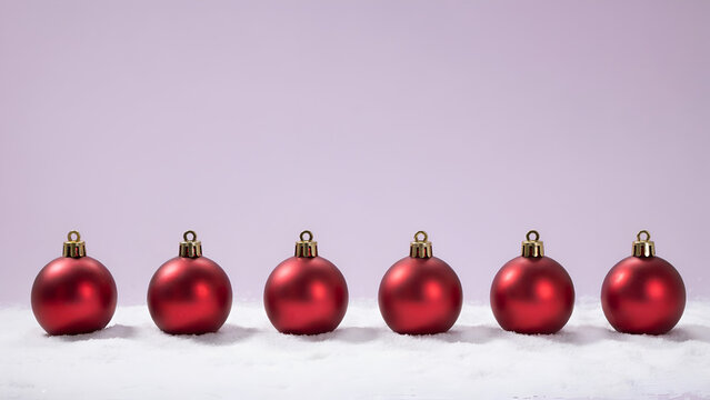 Six red christmas baubles arranged in a row on a snowy surface against a soft purple background