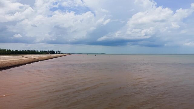People enjoy leisure time at Con Nhan Beach in Vinh Long, Vietnam. The sky is blue with clouds. The waves gently touch the shore. Families and friends gather for fun.