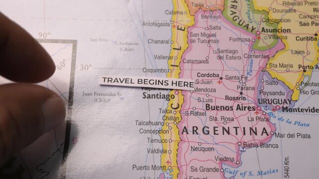 Hand Placing Travel Begins Here Label on South America Map near Santiago Chile