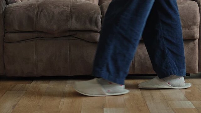 Close-up of feet shuffling and walking back and forth past brown sofa in comfortable house shoes