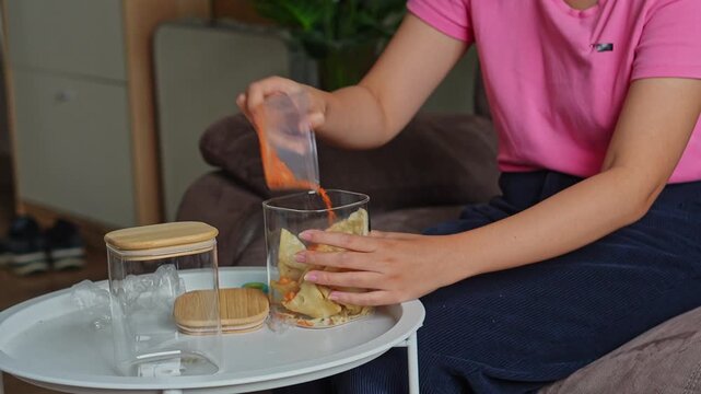Close-up of woman adding chili powder to chips inside clear glass container and shaking to mix