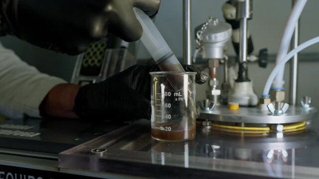 A gloved lab technician precisely transfers a dark organic liquid, likely a biofertilizer or treated waste product, from a syringe into a graduated beaker for quality analysis within a circular agribu