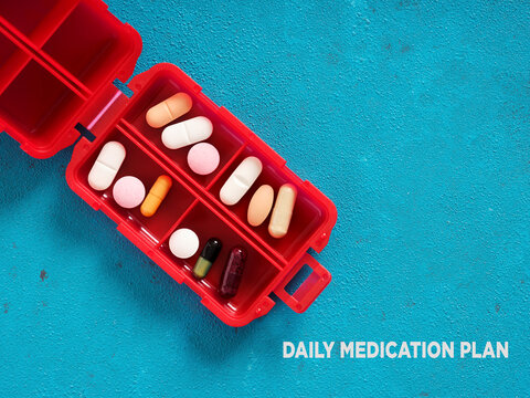 Red pill organizer containing daily medication plan resting on blue background