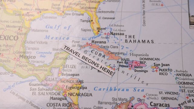 Travel Begins Here paper label placed on a map showing Cuba and Caribbean