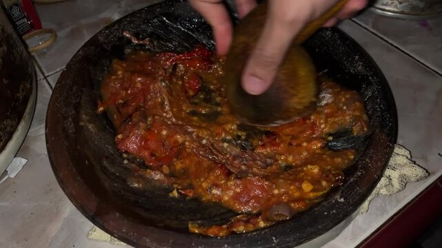 Hand pounding spicy sambal with wooden pestle in mortar
