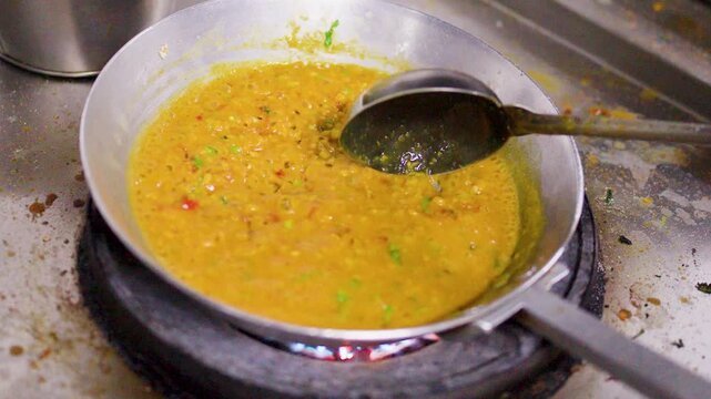 Chef Stirring Yellow Dal Curry with Metal Ladle in Commercial Kitchen