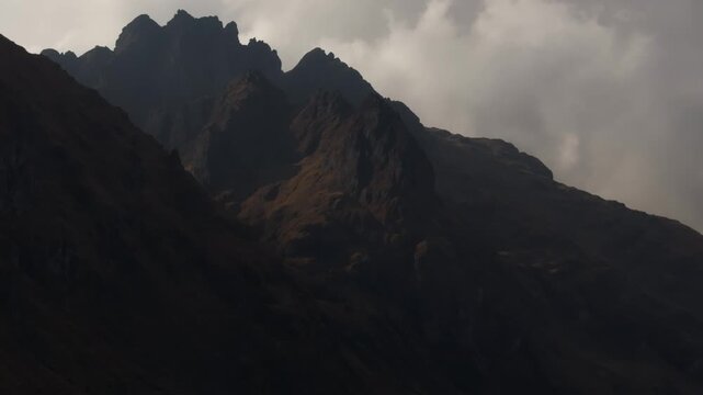 Dramatic close-up view of jagged, shadowed mountain peaks and rugged rocky ridges rising into dense storm clouds in the Peruvian Andes mountain range, Peru.