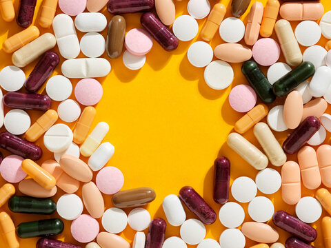 Colorful pills and capsules forming a circle on yellow background