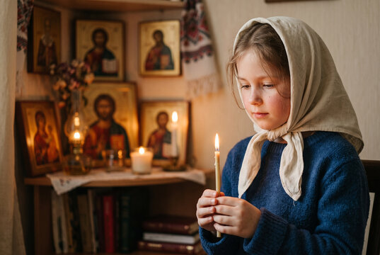 Young girl holding a candle in a dimly lit room with icons  