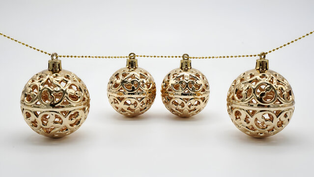 Four decorative gold christmas baubles with intricate filigree patterns hanging on a golden beaded string isolated on white background