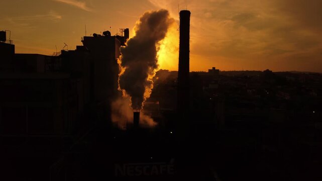 Aerial view of the Nescafe factory with a tall chimney emitting smoke against a vibrant sunset sky in Araras, Sao Paulo, Brazil.