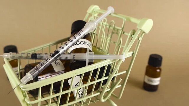 Miniature shopping trolley containing vaccine vials and syringes turning slowly, symbolizing the pharmaceutical business, healthcare costs, and the global distribution of immunization drugs