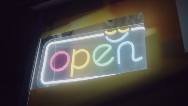 Pastel retro LED Open sign glows behind a shop window at night, soft warm light and shallow focus creating a cozy mood for small business, retail, cafe and bar marketing.