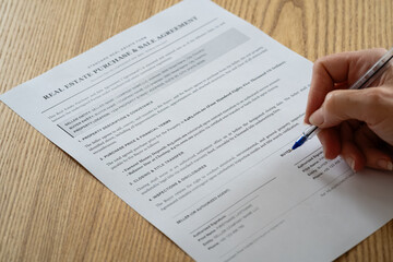 Fototapeta premium Person signing real estate purchase and sale agreement contract on wooden desk close up 