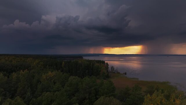 Storm with lightning over the lake. Aerial view of the coast of the lake with the stormy clouds forming in the sky, rain falling on the horizon and lightning flashing. The Kama river, Russia