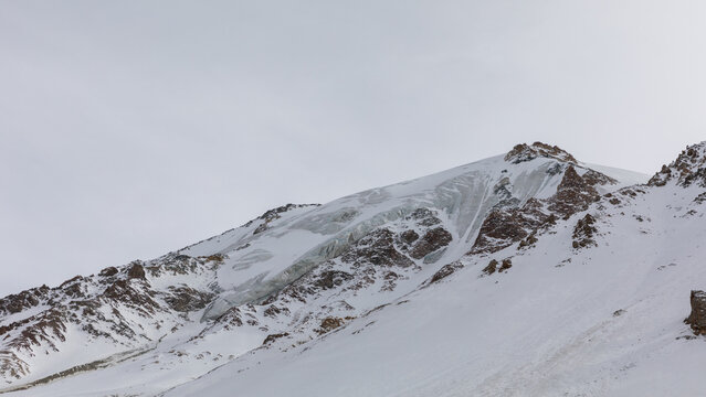 Wide winter view of snow covered rocky peaks and a glacier on Arabel Plateau, Tian Shan mountains, Issyk Kul Region, Kyrgyzstan under an overcast sky