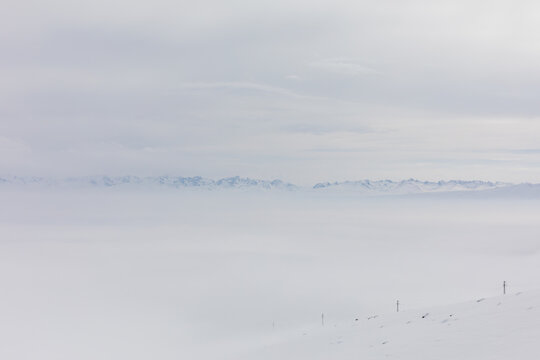 Minimalist winter landscape at Ala-Bel Pass, Kyrgyzstan, with a wide layer of fog, snowy slopes and distant mountain ridge under an overcast sky