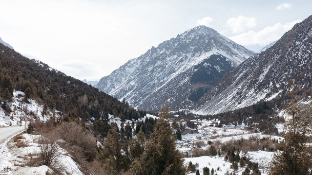 Snowy mountains and forested valley in Ala Archa National Park near Bishkek, Chuy Region, Kyrgyzstan, with winding road and dramatic peaks in winter