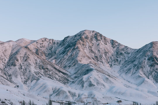 Wide view of snow-covered mountain ridges and rocky peaks under a pale blue sky at dusk in Chunkurchak Valley, Chuy Region, Kyrgyzstan