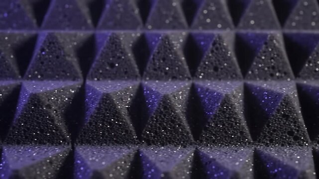 Close up macro shot of dark acoustic foam panels with geometric pyramids glowing under purple studio light