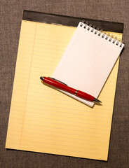 Yellow legal pad with small notebook and red pen on textured surface © Firnthirith