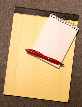 Yellow legal pad with small notebook and red pen on textured surface