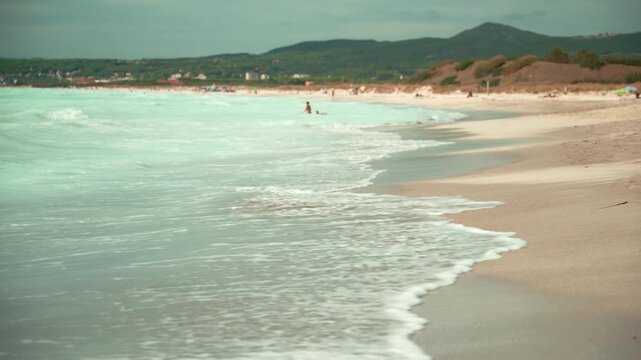 Spiagge Bianche, Italy. Stunning seascape of an italian beach with turquoise water and gentle waves lapping the shore, tourists swimming and relaxing under a cloudy sky with hills in the background