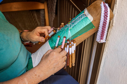 Close up of a woman making traditional handmade bobbin lace using wooden bobbins and a lace pillow.