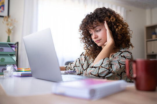 White woman with curly hair working on laptop at home office desk