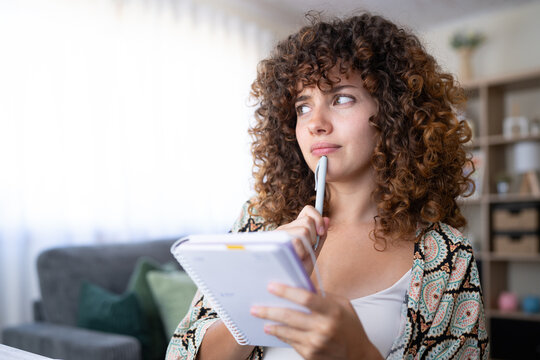 White girl thoughtfully holding pen and notebook at home in Spain