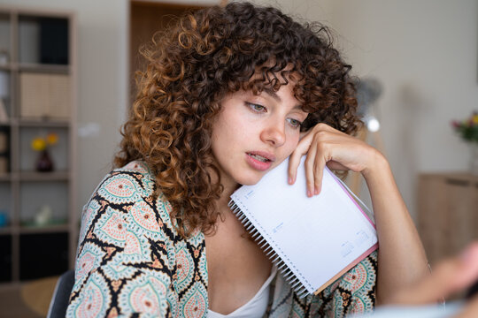 White woman holding notebook thoughtfully at home in Spain