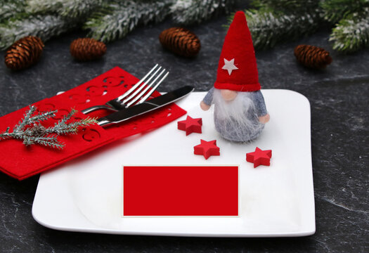 A festive Christmas table setting featuring a St Nicholas elf, a square plate, a red felt cutlery pouch and a blank red place card for you to write your own message on.