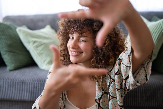 White woman with curly hair winking and framing face indoors