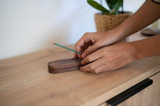 Hands placing an incense stick in wooden holder on table